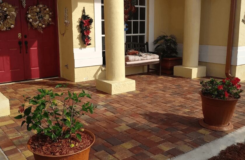 Red brick paver patio in front of yellow house with red door