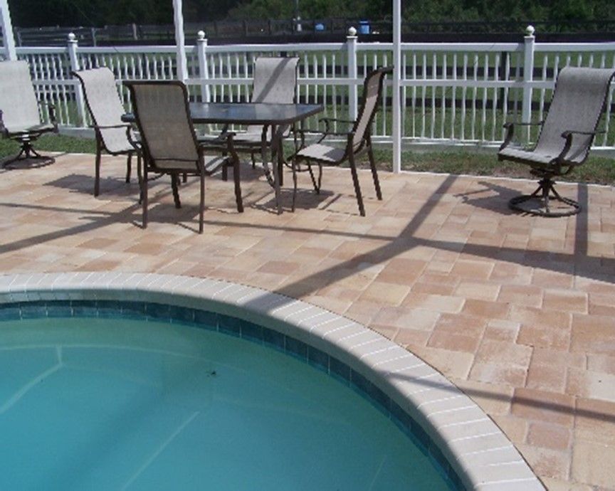 Tan brick pavers pool deck next to pool with patio chairs